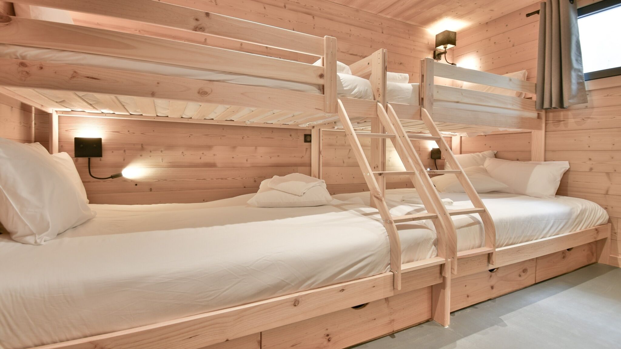 A wooden cabin-style room with bunk beds, a ladder, and a wall-mounted light fixture.