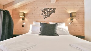 Een slaapkamer met een houten plafond, een bed met wit en grijs beddengoed, twee wandlampen en een decoratief object aan de muur.