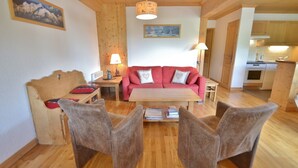 A cozy living room with a wooden ceiling, a red sofa, a wooden table, and two armchairs. - Refuge les Echelles E4 (Le Grand Bornand)