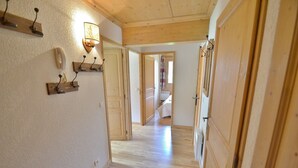 A hallway with wooden floors and walls, leading to a bedroom with a bed and a window. - Refuge les Echelles E4 (Le Grand Bornand)