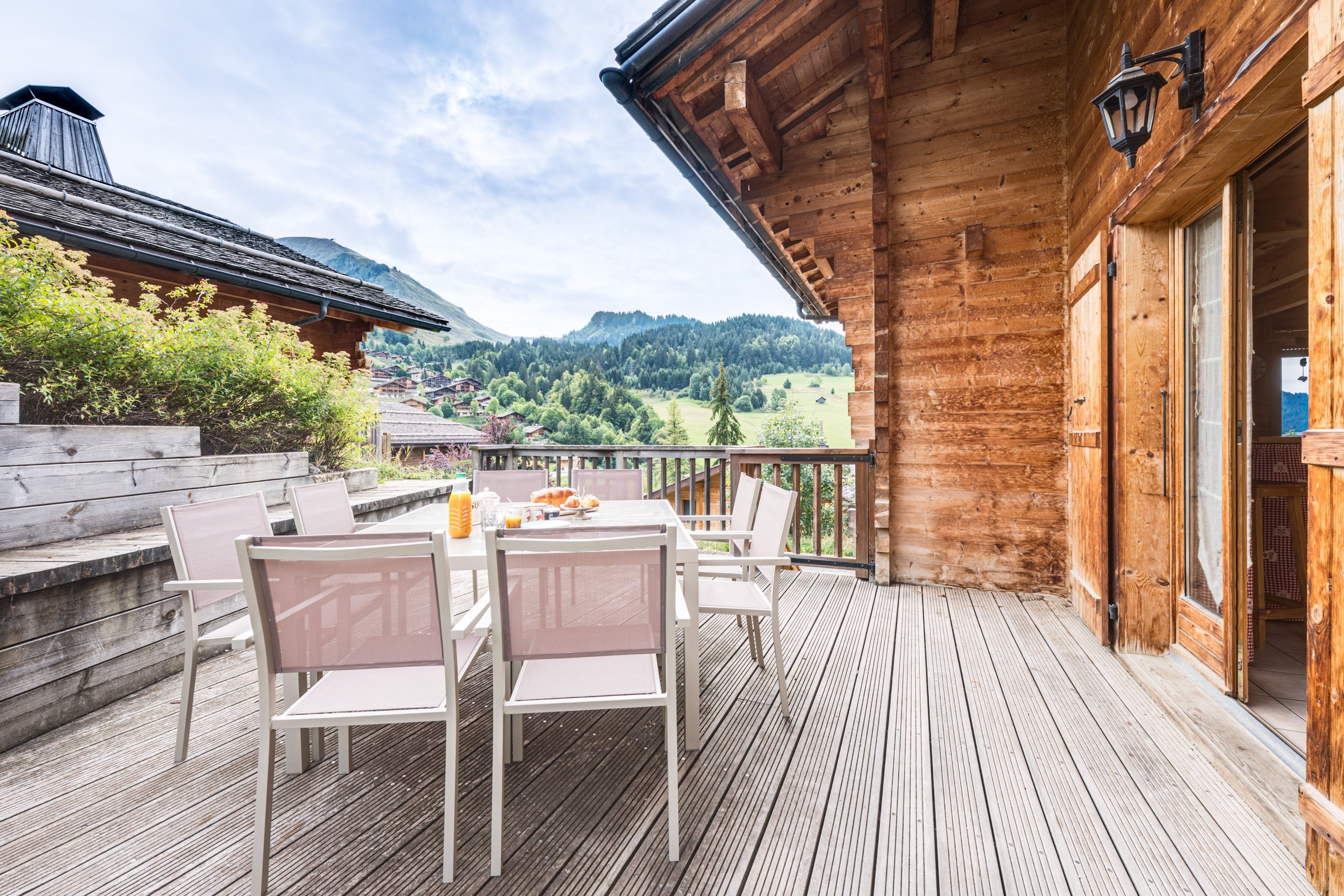 A wooden deck with a table and chairs, overlooking a mountainous landscape.
