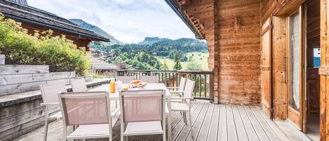 A wooden deck with a table and chairs, overlooking a mountainous landscape.