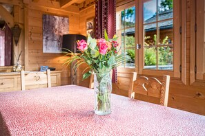 Un interior de madera con una mesa lista para comer, un florero con flores y una ventana con vistas al verdor.