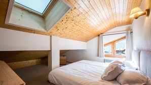 Une chambre avec un plafond en pente, un puits de lumière, un lit avec des oreillers et une table de chevet.