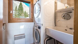 Un espace buanderie compact comprenant un lave-linge et un sèche-linge à chargement frontal, un petit évier et une fenêtre donnant sur des arbres et des montagnes.