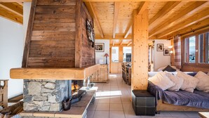 Un intérieur de chalet chaleureux avec une cheminée en pierre, des poutres en bois, un canapé et un coin repas.
