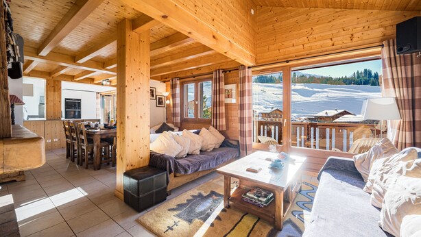 L’intérieur d’un chalet en bois comprend un coin repas, un canapé et offre une vue sur un paysage enneigé.