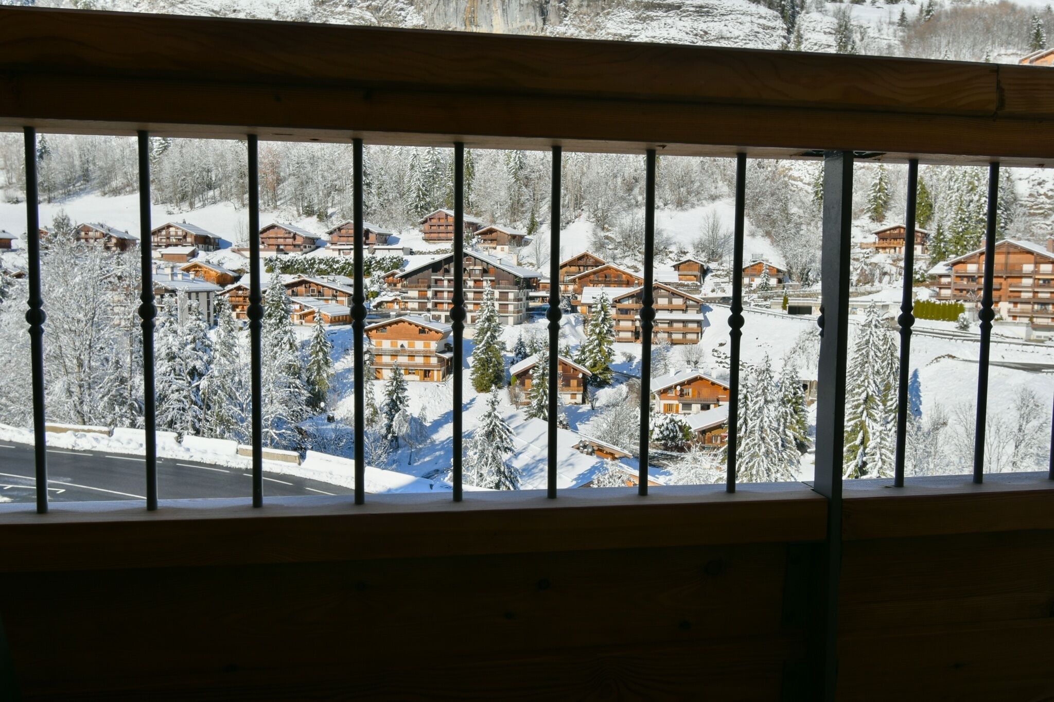 A view of a snow-covered village with wooden buildings, a road, and a railway track.