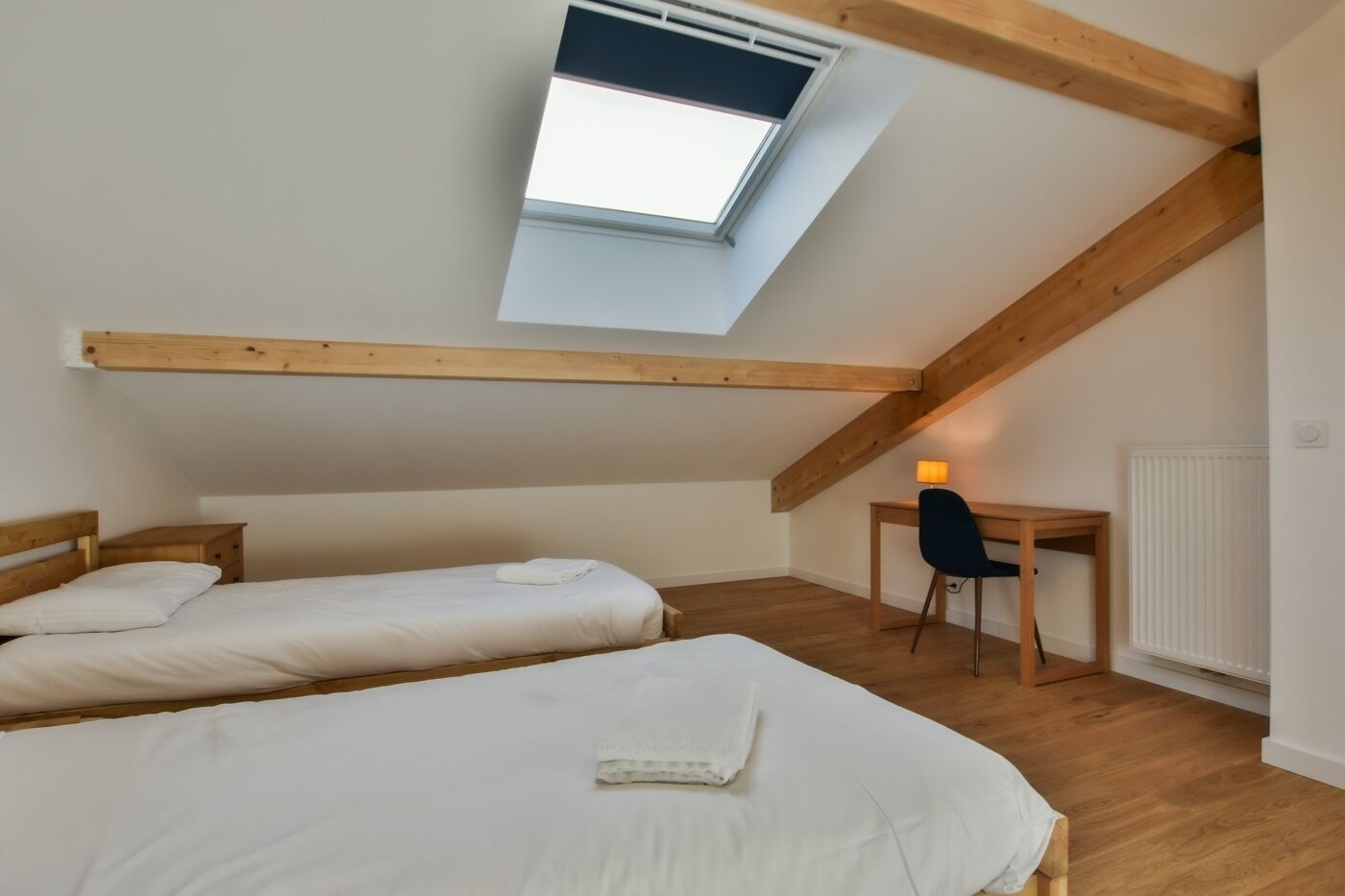 Une petite chambre agréable, dotée de deux lits simples, d’un bureau avec une chaise et d’une lucarne.