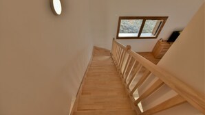 A wooden staircase with a handrail, a small window with a view, and a wall-mounted light fixture. - Le Sève C201 - Three Bedroom Apartment, Sleeps 6 (Samoëns)