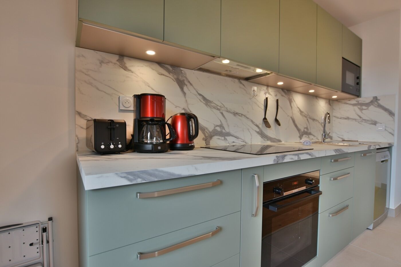 A modern kitchen with marble backsplash, stainless steel appliances, and light green cabinetry.