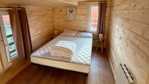 Une chambre dans une cabane en bois, avec un lit, un radiateur et une fenêtre avec des rideaux.