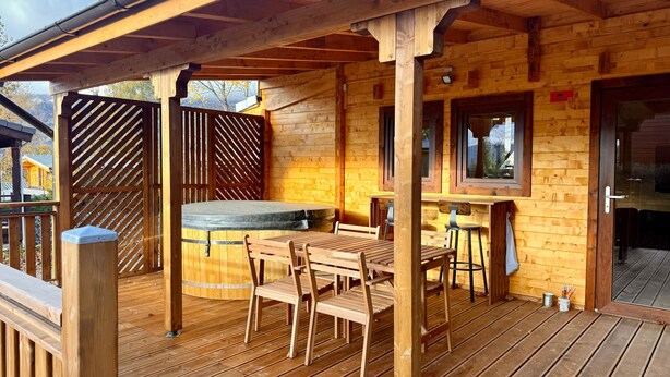 Une terrasse en bois avec une table et des chaises, un jacuzzi et un coin bar.