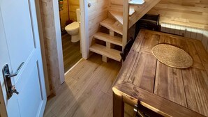 Un intérieur en bois avec un escalier menant à un niveau supérieur, une table à manger avec un set de table en fibres tressées et une porte blanche.