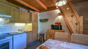 A kitchen with wooden cabinets, a stove, and a dining area with wicker chairs. - Refuge Les Echelles E6 (Le Grand Bornand)