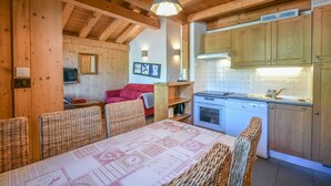 A cozy cabin interior with a dining area, kitchen, and a red sofa. - Refuge Les Echelles E6 (Le Grand Bornand)
