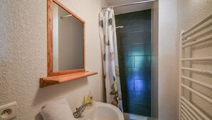 A bathroom with a white sink, a wooden shelf above it, a towel, a mirror, and a shower with a curtain. - Refuge Les Echelles E6 (Le Grand Bornand)