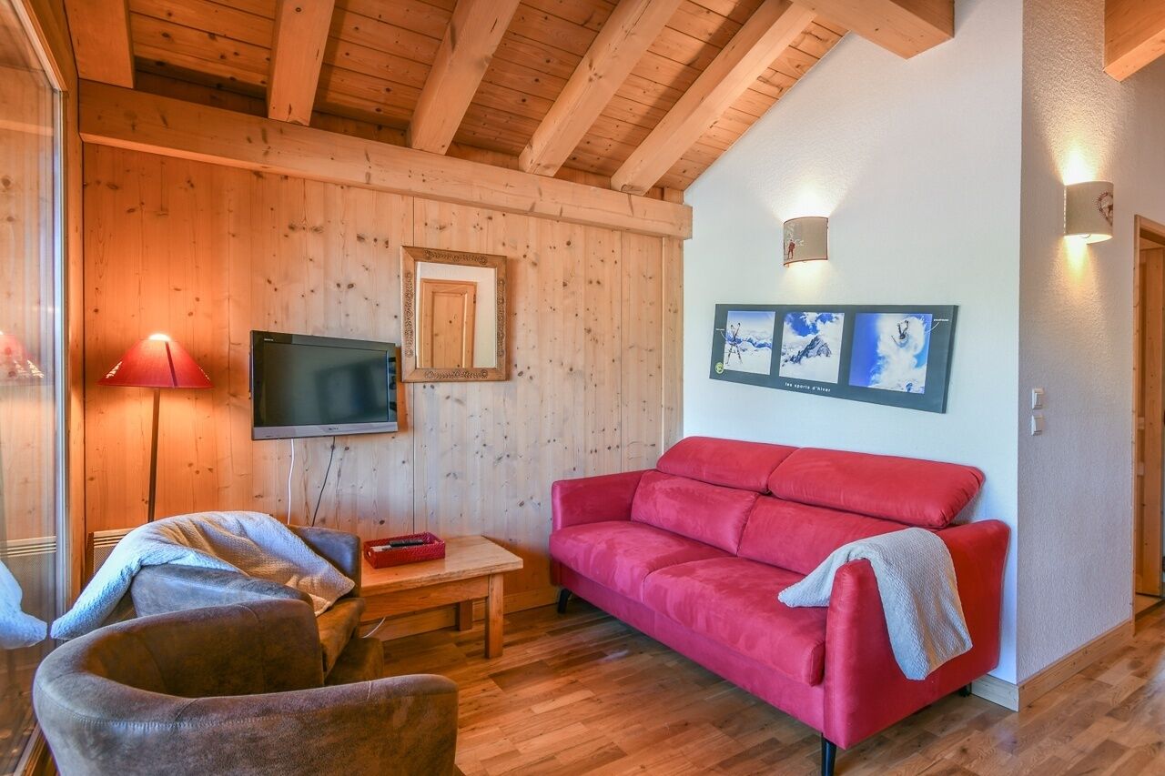 A cozy room with wooden walls, a red sofa, a television, and framed pictures on the wall.