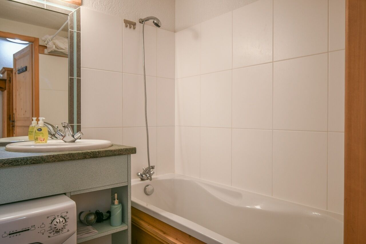 A bathroom with a white bathtub, a sink with a mirror, and a showerhead.