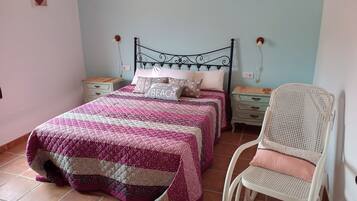 A bedroom with two beds, a white chair, and a nightstand with a lamp.