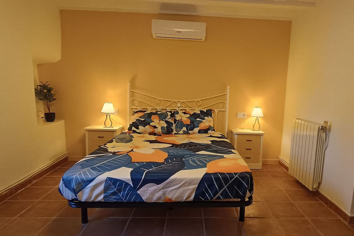 A bedroom with a bed, two bedside tables with lamps, a radiator, and a potted plant.