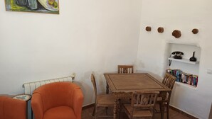A dining area with a wooden table and chairs, a small orange sofa, a radiator, and a shelf with books and a telephone. - El Oasis Morado (Lorca)
