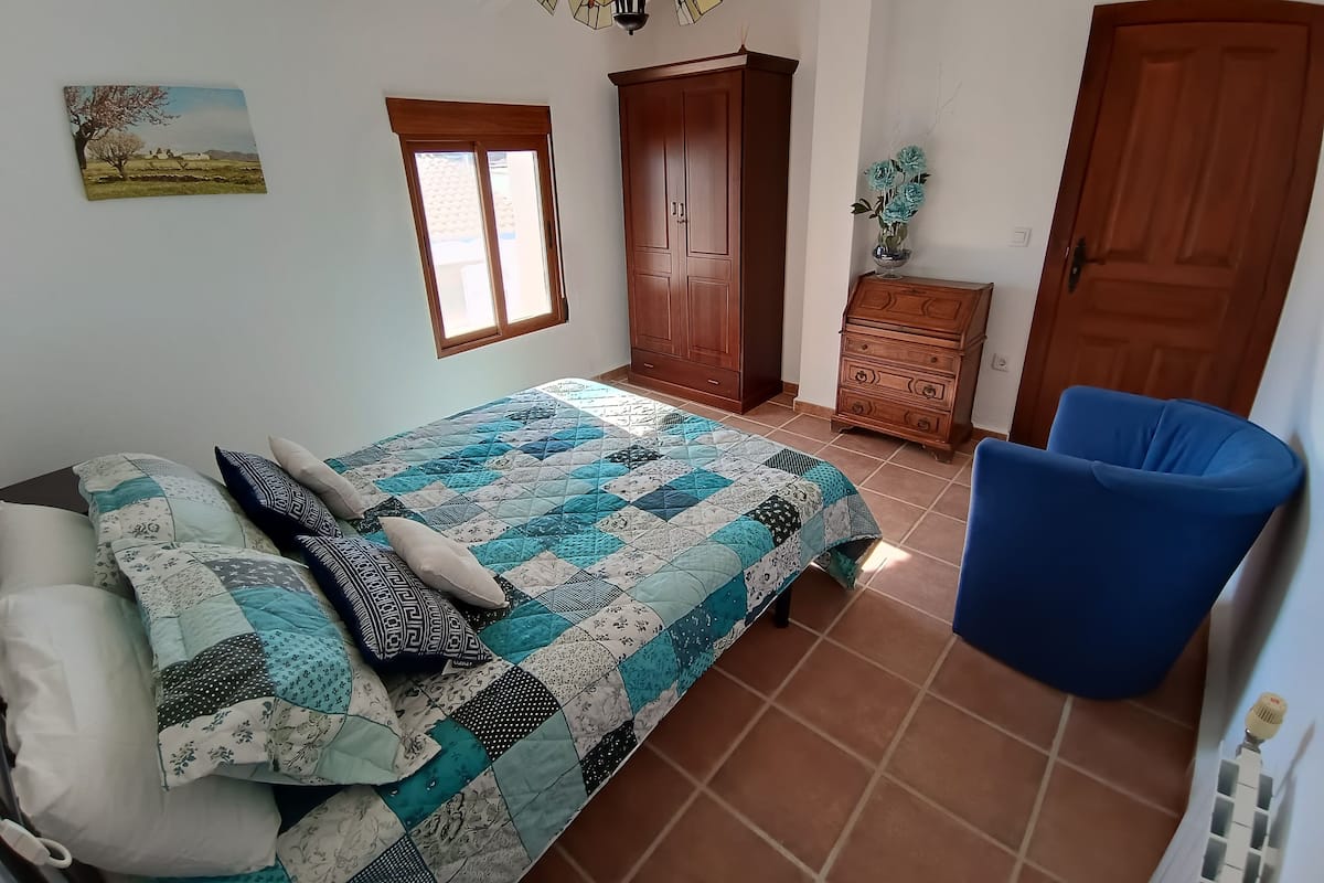 A bedroom with a bed, a chair, a wardrobe, a dresser, and a window.