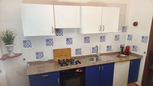 A kitchen with white cabinets, blue accents, a gas stove, a sink, and a red blender. - El Oasis Morado (Lorca)