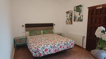Een slaapkamer met een bed, nachtkastje, dressoir en een deur.