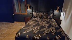 A bedroom with a bed featuring a leaf-patterned bedspread, a dark headboard, and bedside lamps. - El Oasis Morado (Lorca)