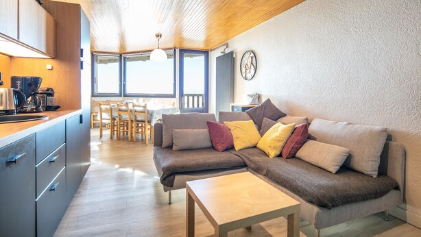 A modern living room with a sofa, coffee table, and kitchen area. - Panoramic 505 - Vue sur la chaîne du Vercors (Chamrousse)