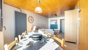 A dining area with a round table, chairs, a clock, and a television in the background. - Panoramic 505 - Vue sur la chaîne du Vercors (Chamrousse)