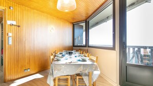 A dining area with a wooden paneled wall, a table set with dinnerware, and a large window offering a view. - Panoramic 505 - Vue sur la chaîne du Vercors (Chamrousse)