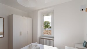 A bedroom with a bed, a window, a radiator, a wardrobe, and a bedside table.