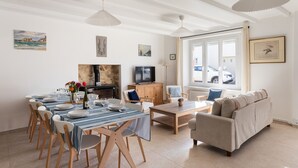 A spacious living area with a dining table set for six, a sofa, a TV, and artwork on the walls.