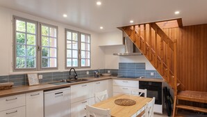 A modern kitchen with white cabinetry, a wooden staircase, and a dining area with a wooden table and chairs.
