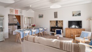 A spacious living room with a sofa, dining table, and chairs. A television and fireplace are visible in the background.