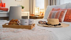 Una cama bien hecha con una bandeja de cruasanes y tazas de café, un sombrero de paja y un par de gafas de sol sobre una manta blanca y esponjosa.