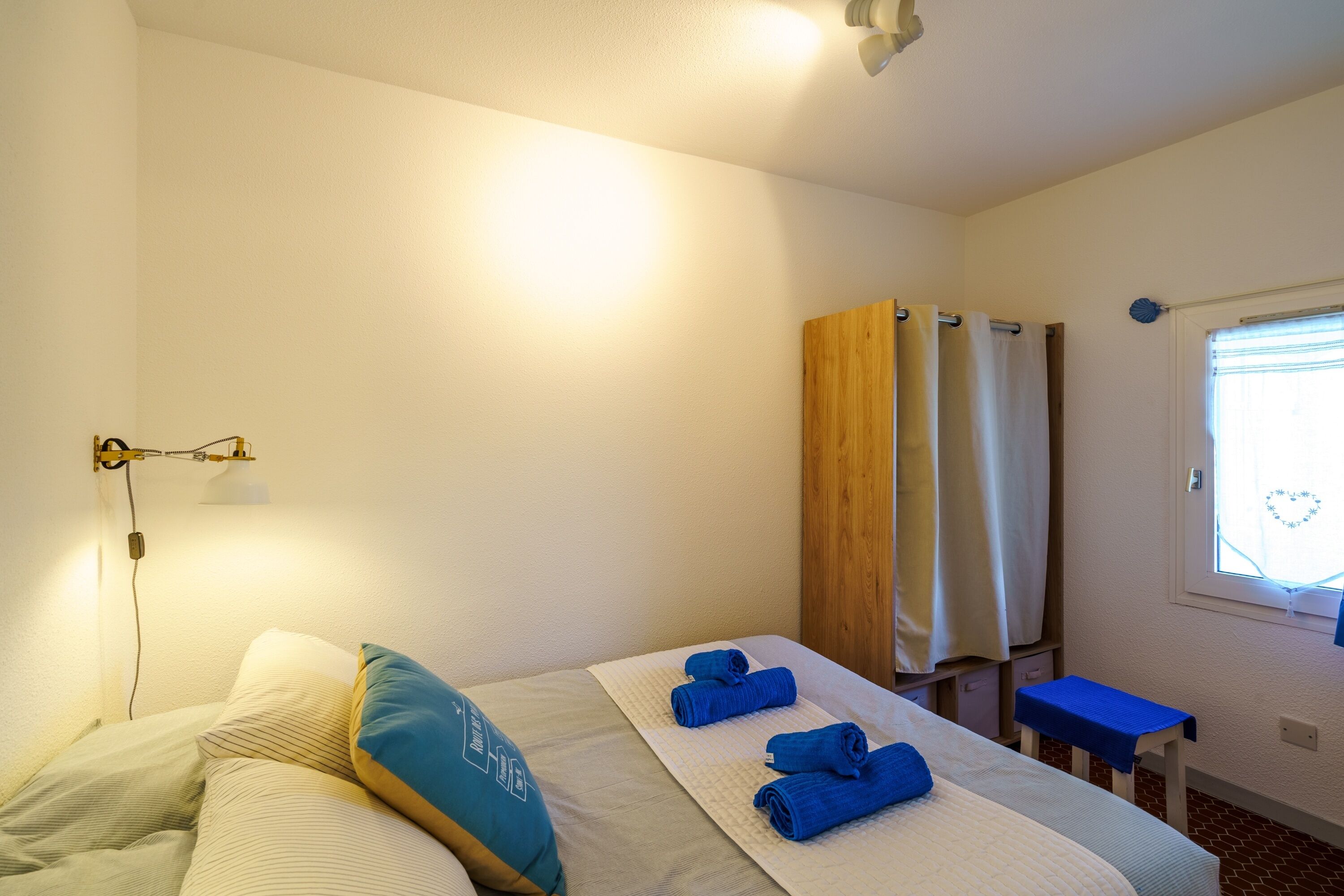 A hotel room with a bed, a bedside table, a window with curtains, and a shower area.