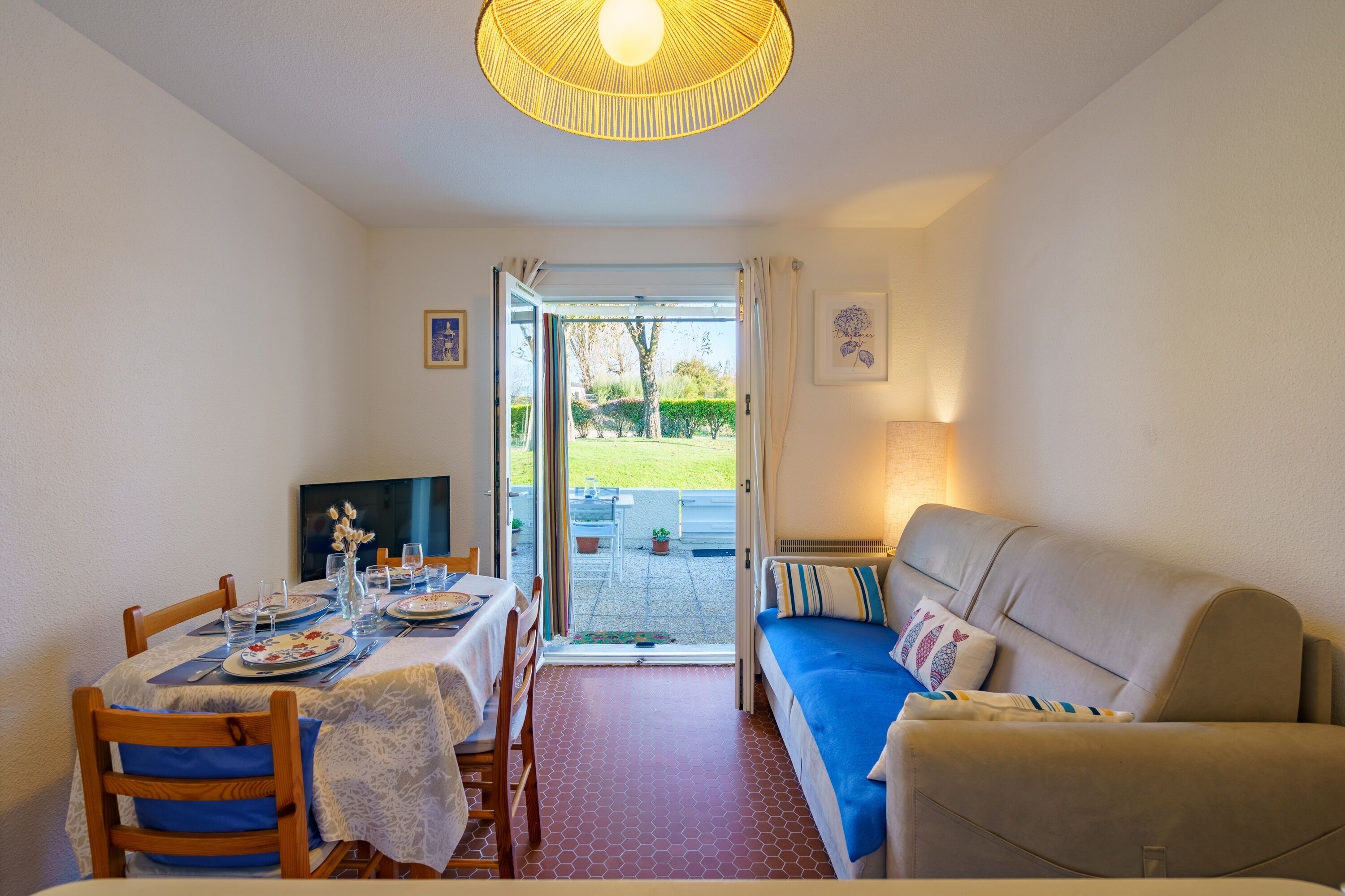 Un coin repas avec une table dressée pour quatre personnes, un canapé et un téléviseur.