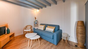 Un salon avec un canapé bleu, une petite table ronde, un téléviseur posé sur un meuble en bois et un grand lampadaire à pied en fibres tressées.