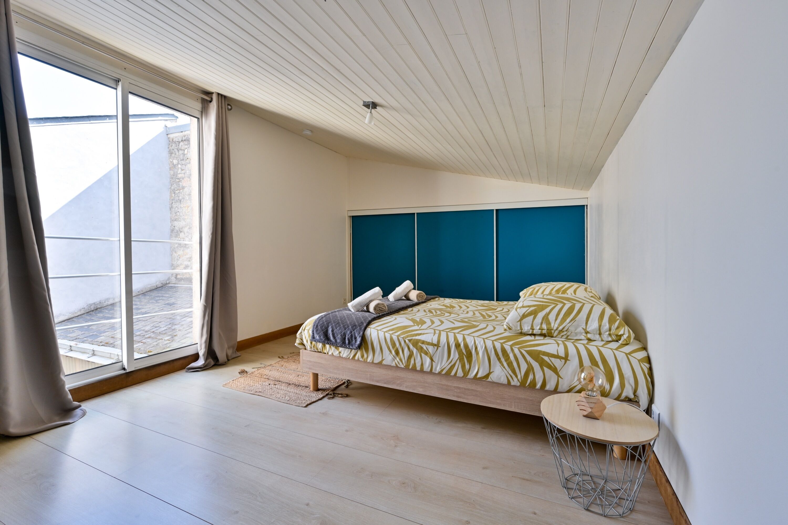A modern bedroom with a bed, a small round table, and a view of the outside.