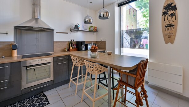 Une cuisine moderne dotée d’une grande cuisinière, d’un four et de luminaires suspendus. On y trouve deux tabourets de bar en bois et une table en bois.