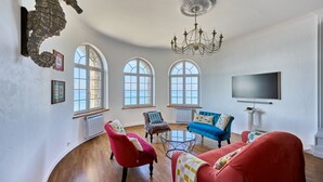 A spacious living room with a curved ceiling, large windows, a chandelier, and a mounted seahorse decoration.