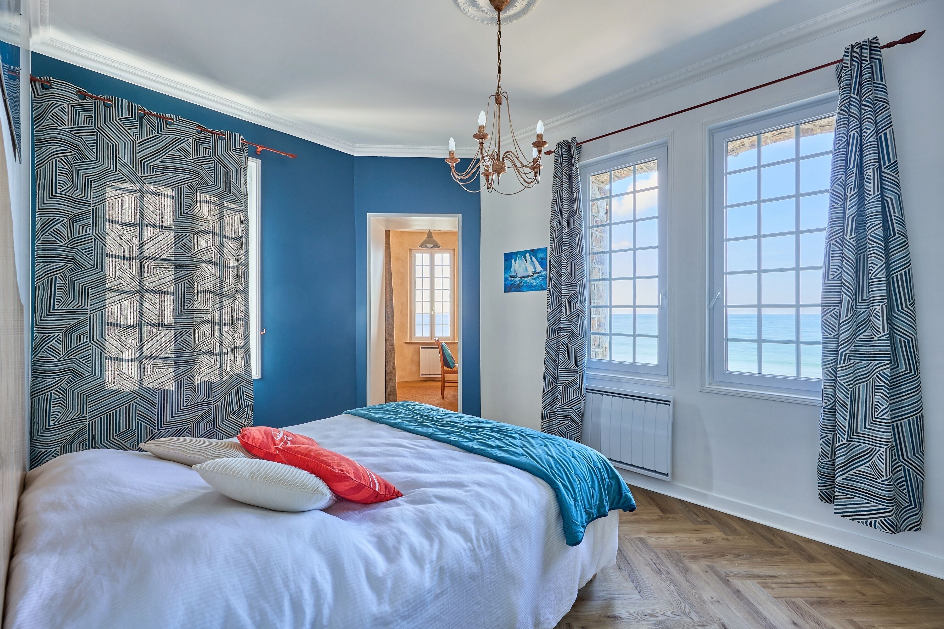 Une chambre avec un grand lit, des rideaux à motifs, un lustre et une vue sur l’extérieur.