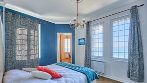 A bedroom with a large bed, patterned curtains, a chandelier, and a view of the outdoors.