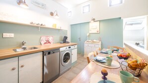 A bright kitchen with a washing machine, sink, and wooden countertop. There are chairs and a table with breakfast items. - Le Baiser du Soleil - Piscine Privée (Mirabel-aux-Baronnies)