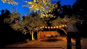 An outdoor patio area with a wooden table and chairs, surrounded by trees and string lights. - Le Baiser du Soleil - Piscine Privée (Mirabel-aux-Baronnies)