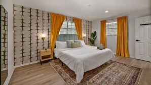Une chambre à coucher moderne avec un grand lit, une table de chevet, une lampe fixée au mur et une porte.
