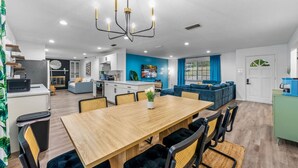 Une cuisine moderne avec des meubles blancs, un coin repas avec une table en bois et des chaises noires, un canapé bleu et un meuble vert.